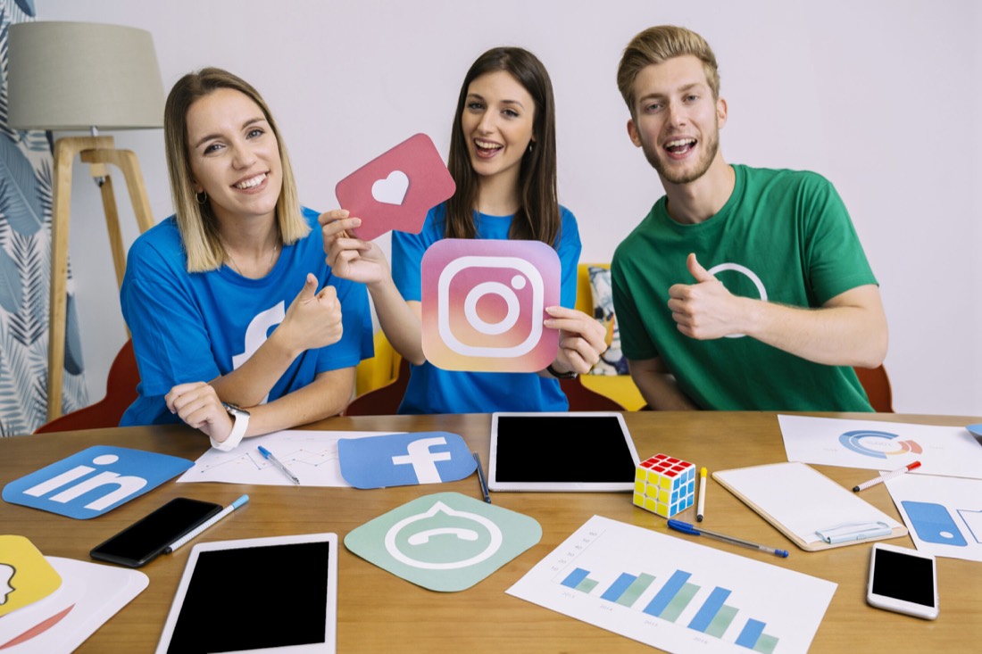 Marketing team holding social media icon cutouts at a desk covered with platform logos and analytics